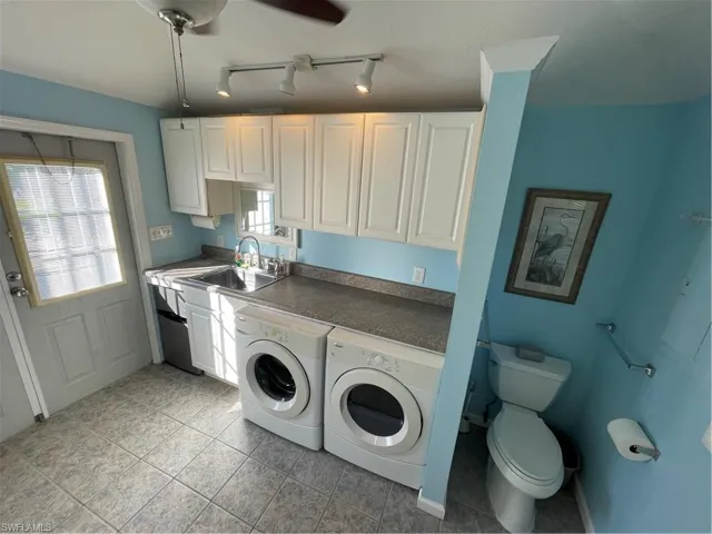 Kitchen featuring white cabinets, washer and clothes dryer, dark countertops, rail lighting, and light tile patterned floors