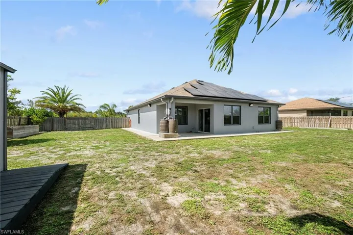 Rear view of property with solar panels, a lawn, and a patio