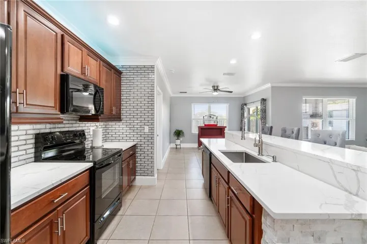Kitchen with custom crown molding, custom backsplash, under & over cabinet lighting, black appliances, and light tile flooring