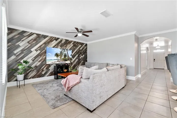 Living room featuring ceiling fan, light tile floors, and crown molding