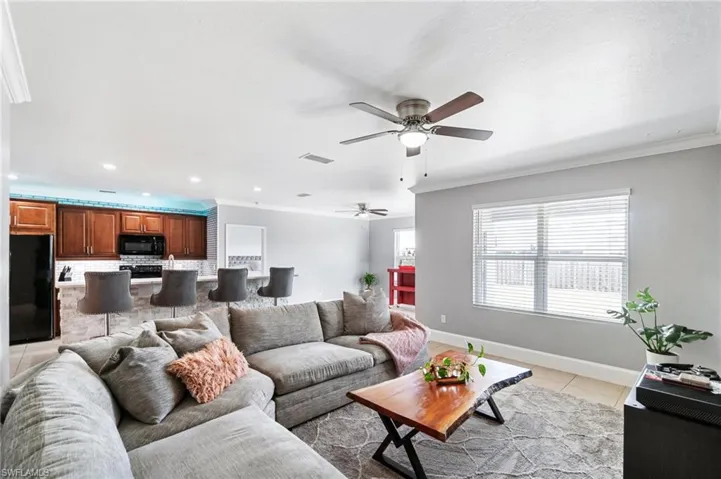 Big open living area featuring crown molding, ceiling fan, neutral tile floors and large window overlooking back patio