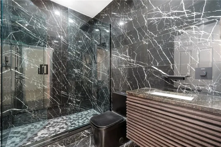 Custom bathroom featuring tile walls, glass shower, sleek black toilet, custom vanity with waterfall faucet