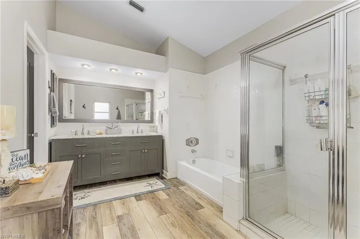 Primary Bathroom featuring double vanity, separate shower and tub, hardwood / wood-style flooring, and lofted ceiling