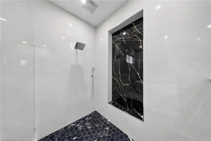 Shower enclosure featuring white marble-look wall tiling, a black hexagonal tile floor, and a recessed niche with black and gold vein-patterned stone