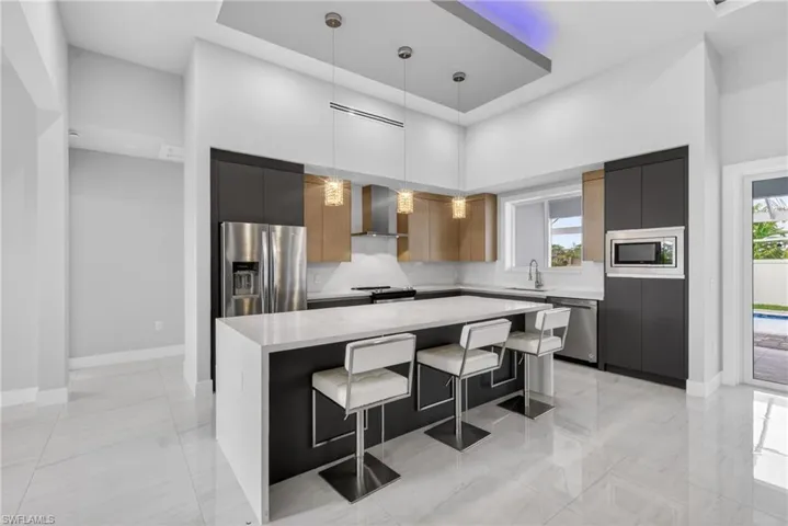 Modern kitchen featuring a large central island with a light-toned countertop, stainless steel appliances, and a recessed ceiling detail with accent lighting