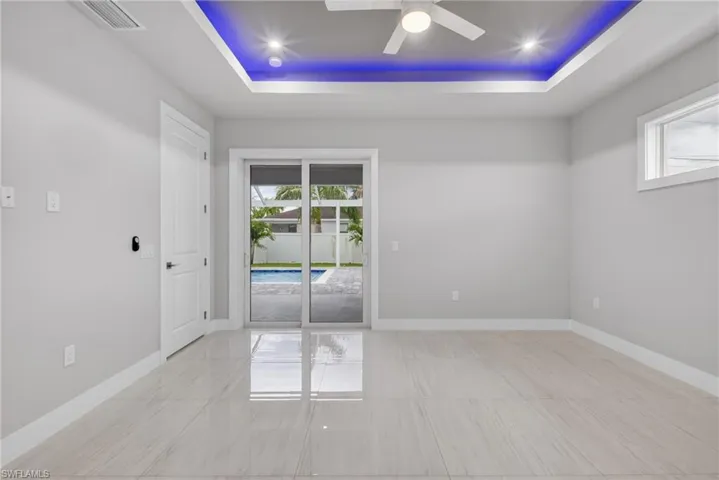 Spacious room featuring large format tile flooring, a tray ceiling with recessed lighting and accent lighting, and a ceiling fan