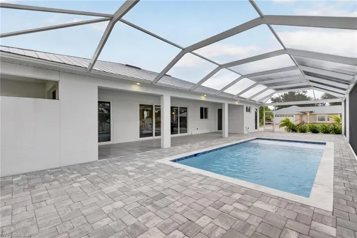 Screened pool enclosure with a rectangular swimming pool, paver deck, and white exterior