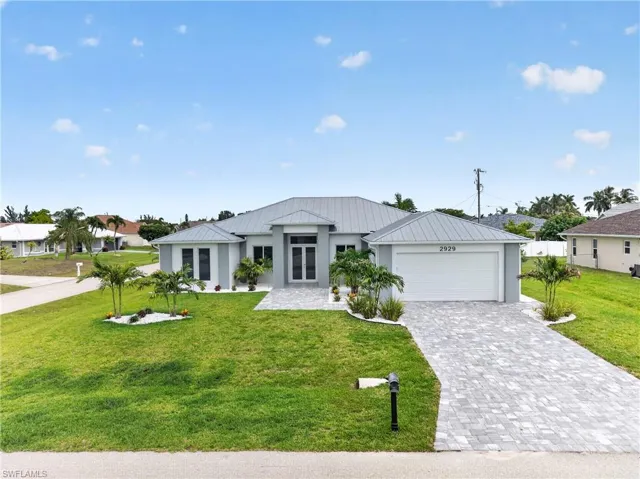 Contemporary single-story residence featuring a light gray exterior, a metal roof, and a paver driveway