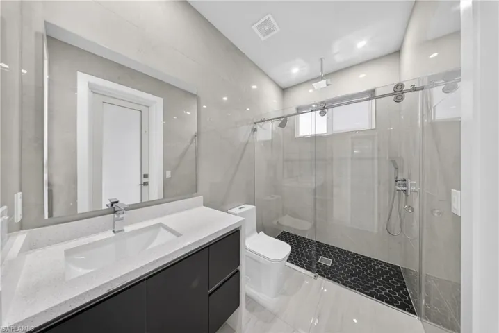 Modern bathroom featuring a single vanity with dark cabinetry and a light-toned countertop, a rectangular undermount sink, a chrome faucet, and an expansive wall mirror