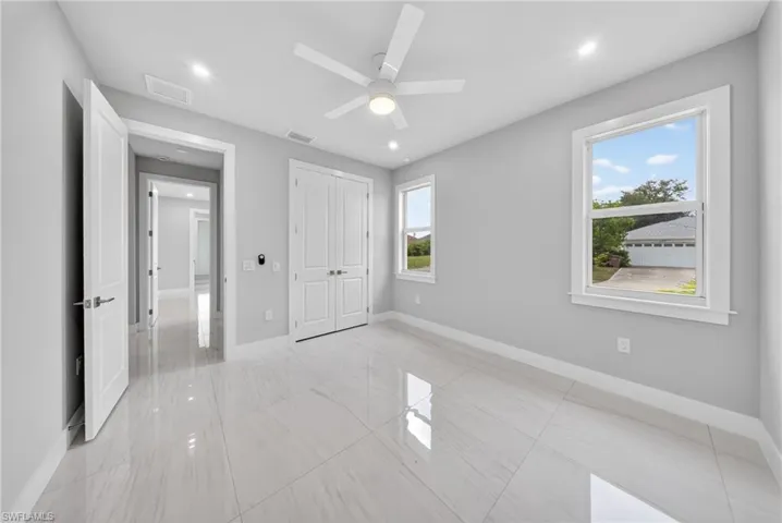 Spacious room featuring large format tile flooring, a contemporary ceiling fan with integrated lighting, two windows with white trim, recessed lighting, and a double-door closet with white paneled doors