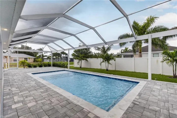 Screened-in outdoor pool area featuring an in-ground swimming pool, a spacious paver patio, and surrounding tropical landscaping
