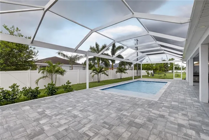 Screened-in pool enclosure featuring a rectangular pool with blue tile accents, surrounded by a paver patio