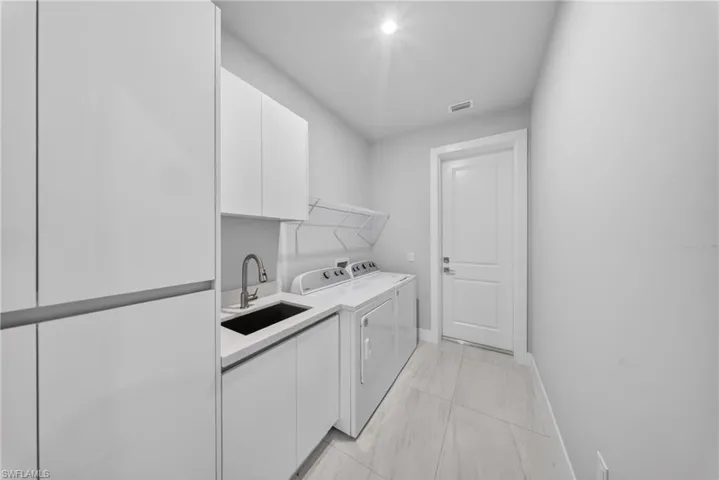 Dedicated utility space featuring a deep black undermount sink with a gooseneck faucet, white flat-panel cabinetry, white countertop, and light-toned tile flooring