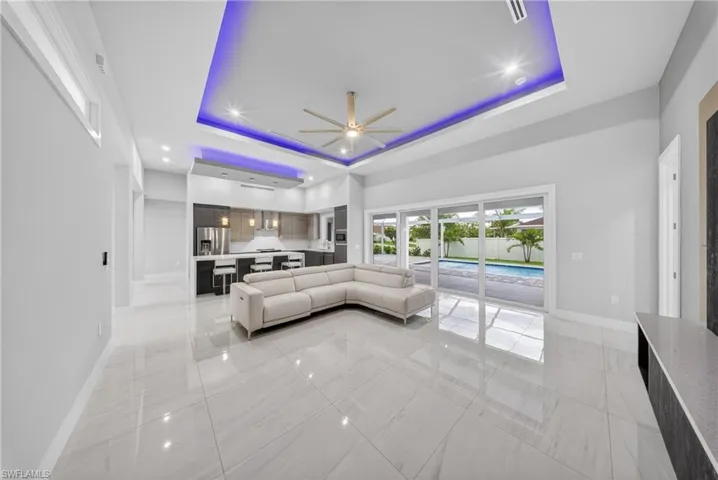 Open concept living space featuring large format porcelain tile flooring, a tray ceiling with recessed lighting and accent lighting, and a modern ceiling fan