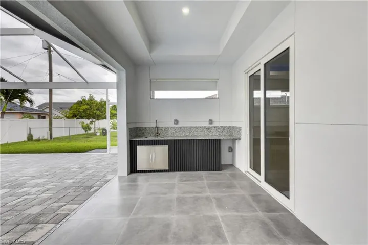 Covered outdoor patio featuring a built-in kitchen area with a sink and under-counter refrigerator
