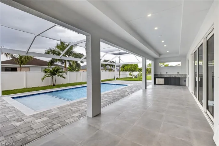 Expansive screened lanai featuring a rectangular swimming pool with integrated spa, paver pool deck, and outdoor kitchen with stone countertop and sink