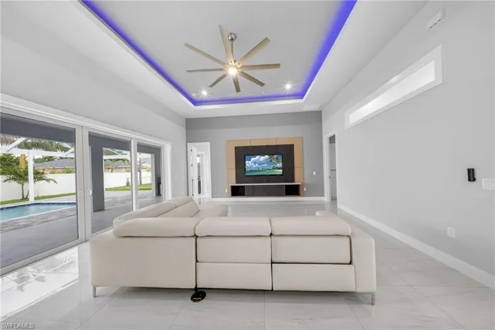 Spacious living area featuring polished tile flooring, a tray ceiling with recessed lighting and accent lighting, and a modern ceiling fan