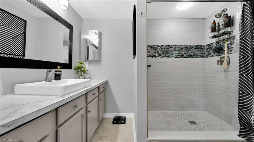 Full bath featuring vanity, tiled shower, light tile patterned floors, and a textured ceiling