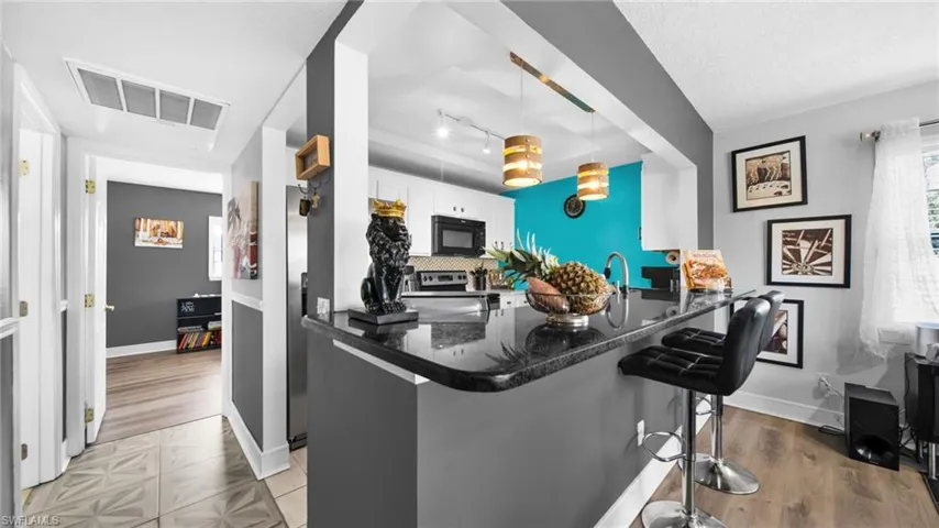 Kitchen featuring a breakfast bar, a peninsula, dark stone counters, black microwave, and white cabinetry