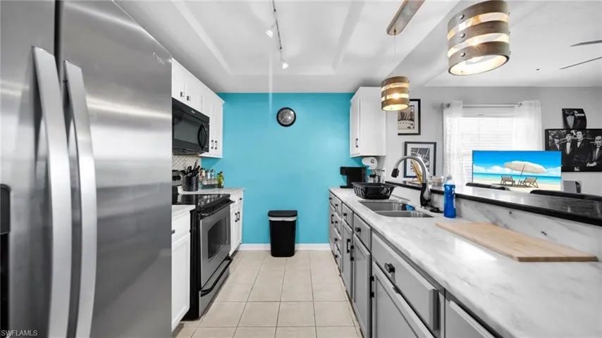 Two tone kitchen featuring stainless steel appliances, dual tone cabinetry, a tray ceiling, track lighting, and light tile patterned floors