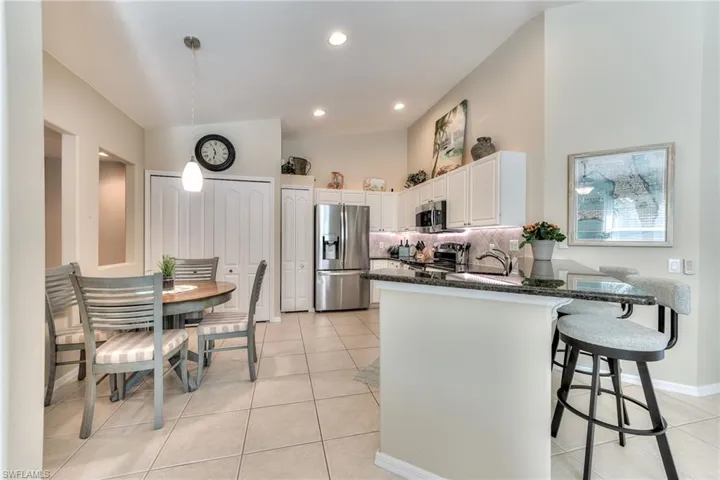 Kitchen with white cabinets, appliances with stainless steel finishes, dark stone countertops, decorative backsplash, and light tile patterned flooring