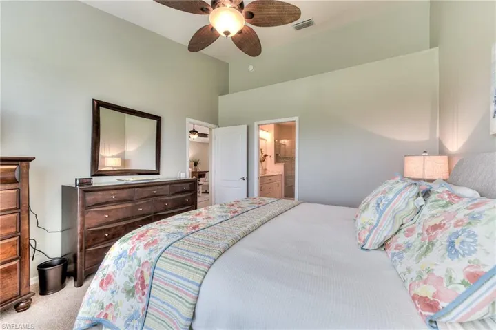Carpeted bedroom featuring ceiling fan, connected bathroom, and vaulted ceiling
