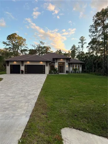 Prairie-style home with a front yard, an attached garage, decorative driveway, and stucco siding