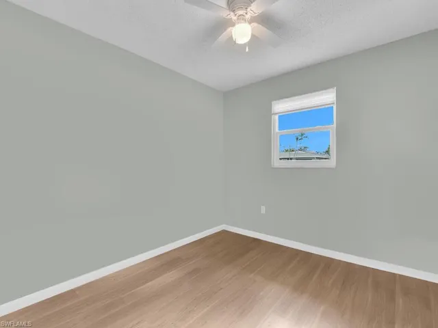 Empty room featuring wood finished floors, baseboards, a ceiling fan, and a textured ceiling