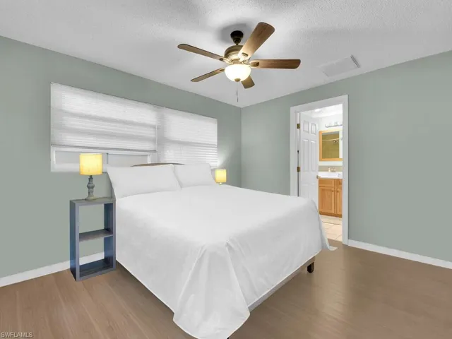 Bedroom with wood finished floors, a textured ceiling, baseboards, and connected bathroom