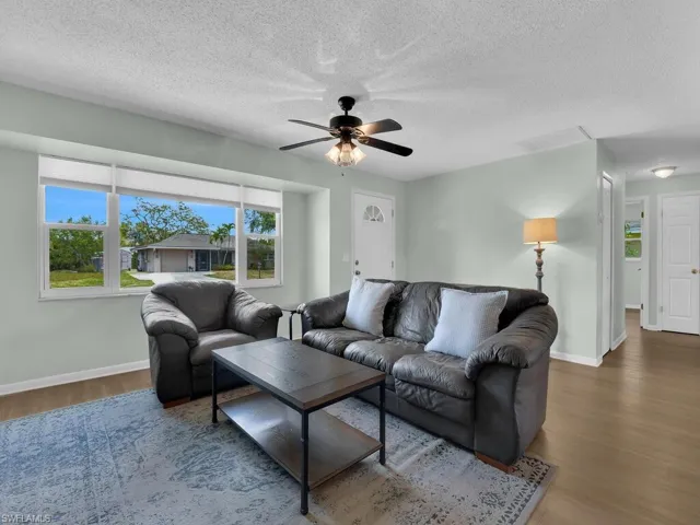 Living area featuring a ceiling fan, wood finished floors, baseboards, and a textured ceiling