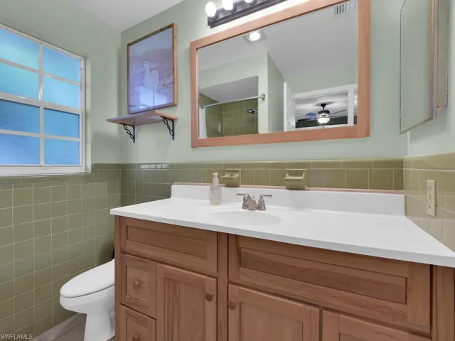 Full bath with a shower, vanity, tile walls, toilet, and ceiling fan