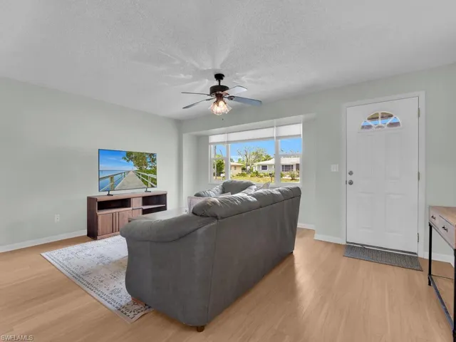 Living area with light wood-style flooring, a ceiling fan, baseboards, and a textured ceiling