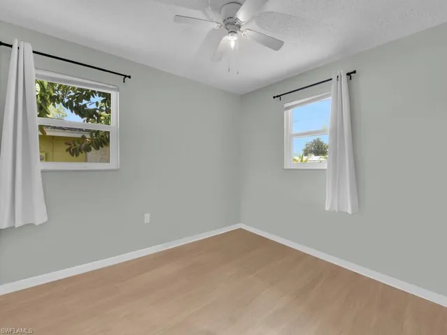 Empty room with wood finished floors, baseboards, a textured ceiling, and a ceiling fan