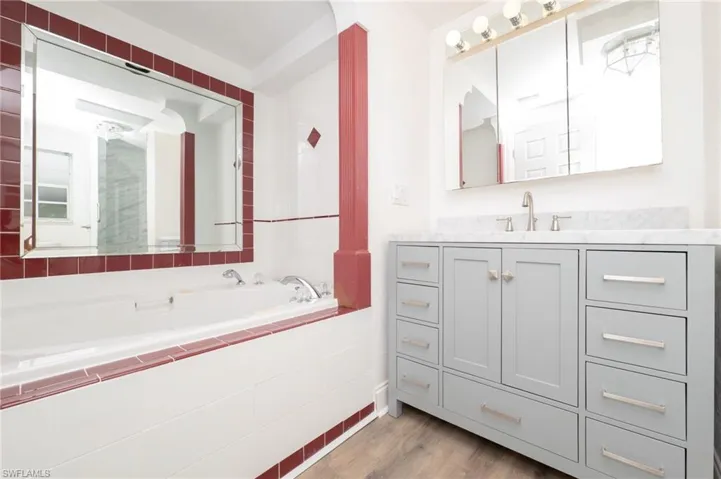 Bathroom with vanity with extensive cabinet space, tiled tub, and hardwood / wood-style flooring