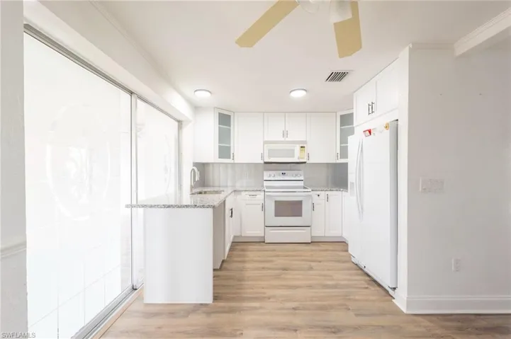 Kitchen with white appliances, white cabinets, light stone counters, and light hardwood / wood-style flooring