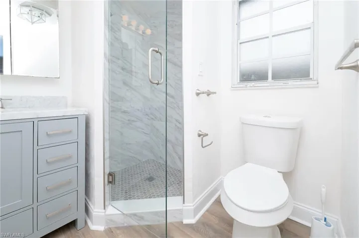 Bathroom featuring large vanity, hardwood / wood-style flooring, toilet, and a shower with door