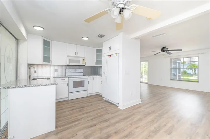 Kitchen with light hardwood / wood-style floors, white appliances, tasteful backsplash, light stone counters, and white cabinets