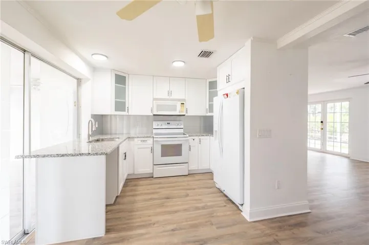 Kitchen with light wood-type flooring, white appliances, white cabinetry, and ceiling fan