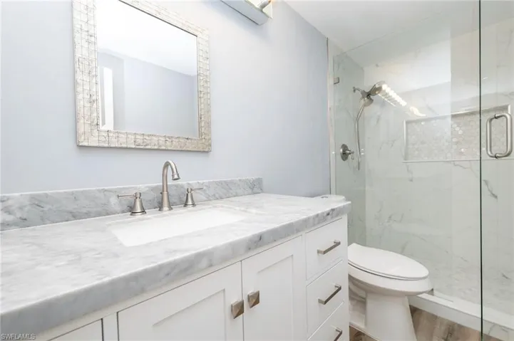 Bathroom featuring wood-type flooring, an enclosed shower, oversized vanity, and toilet