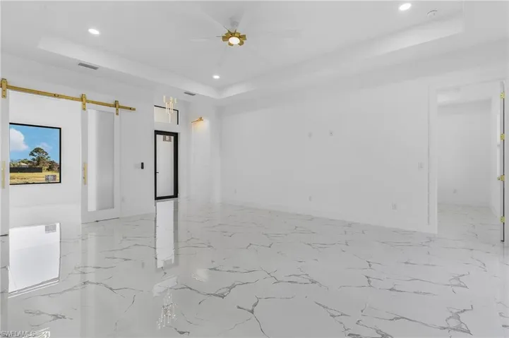 Spare room with a barn door, a tray ceiling, recessed lighting, a ceiling fan, and light marble finish floors