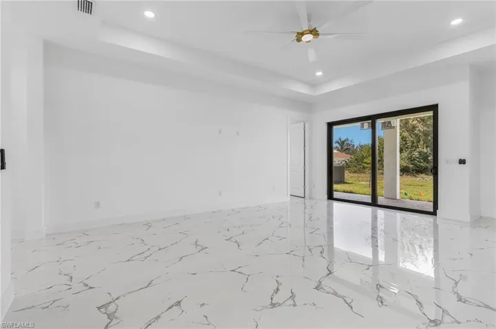 Unfurnished room featuring a raised ceiling, recessed lighting, light marble finish flooring, and ceiling fan