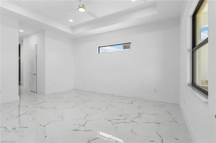 Spare room with a raised ceiling, light marble finish floors, recessed lighting, and a ceiling fan
