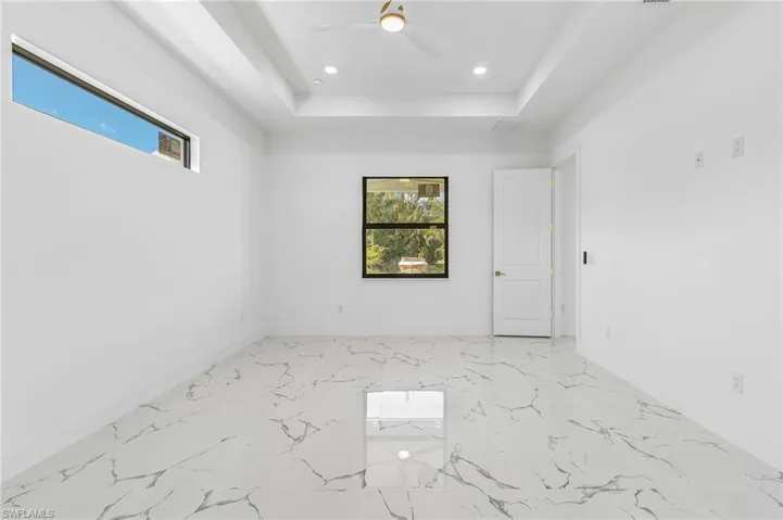 Empty room with light marble finish floors, a raised ceiling, a ceiling fan, and recessed lighting
