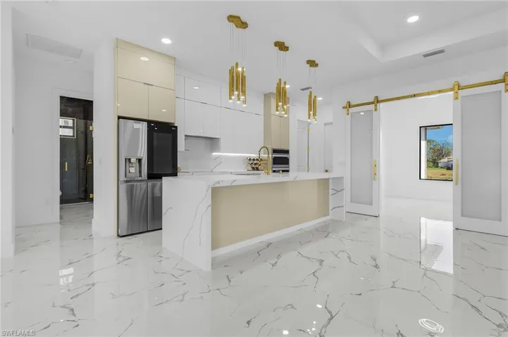 Kitchen with modern cabinets, stainless steel appliances, pendant lighting, light stone countertops, and a barn door