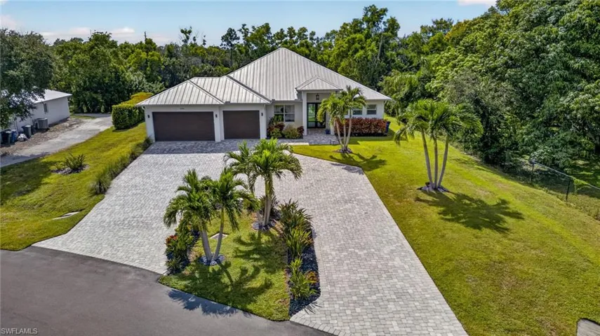 Large circular paver driveway, three-car garage, lush landscaping, and mature palm trees