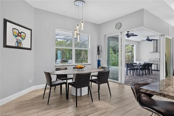Wood-finish flooring, contemporary chandelier, large window, and sliding glass doors leading to an outdoor kitchen area
