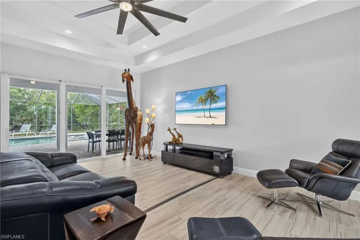 Tray ceiling with recessed lighting and a modern ceiling fan, tile plank flooring, and sliding glass doors opening to an outdoor screened enclosure with a pool and spa