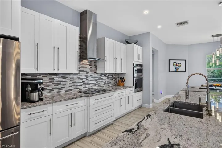 White cabinetry, stainless steel appliances, stainless range hood, mosaic tile backsplash, double basin sink, and pendant lighting