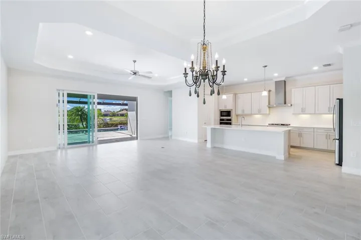 Unfurnished living room with ceiling fan with notable chandelier, sink, a tray ceiling, and light tile flooring