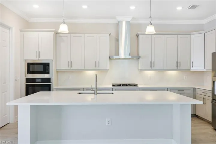 Kitchen featuring black microwave, a center island with sink, wall chimney exhaust hood, oven, and sink